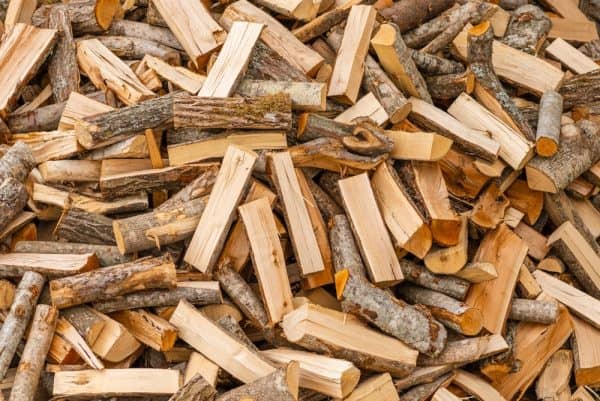 A large pile of Semi Seasoned Firewood (BULK) with various sizes and shapes of logs sits ready, reminiscent of a fresh topsoil delivery in Queens County. The wood pieces, sporting light brown and beige hues with bark on some sides, are haphazardly stacked, filling the entire frame.